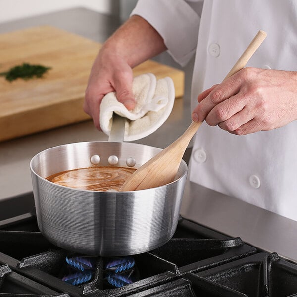 A person stirring soup in a Choice aluminum sauce pan on a stove.