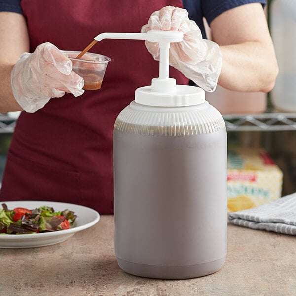 A woman using a Tablecraft condiment pump to pour brown liquid into a white plastic container.