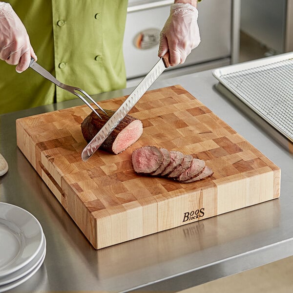 A chef using a knife to cut meat on a John Boos maple wood chopping block.