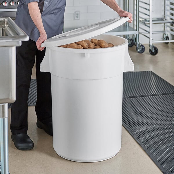 A man putting potatoes in a large white round ingredient storage bin.