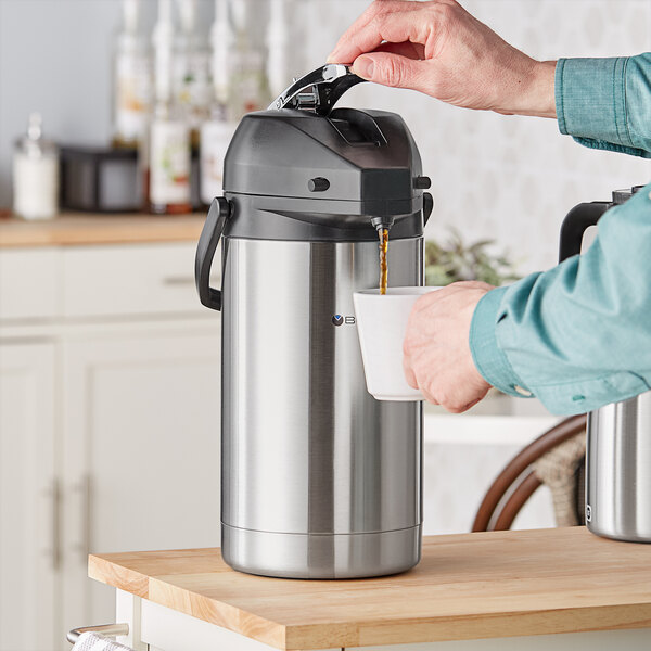 A person pouring coffee into a Bunn stainless steel airpot.