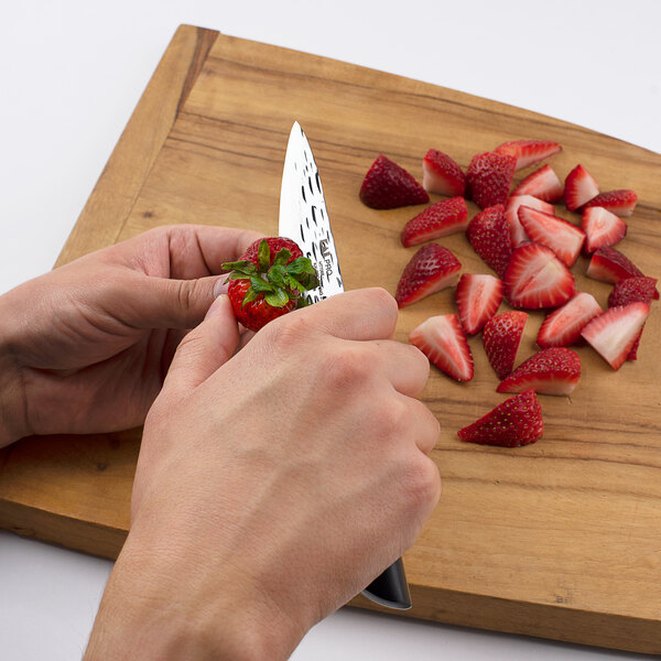 A person using a Kai PRO paring knife to cut strawberries on a cutting board.
