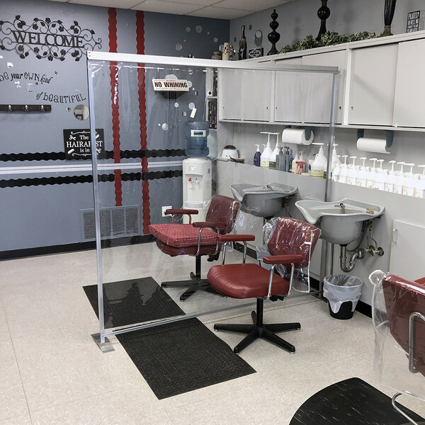 A Goff's clear PVC standing partition with aluminum frame and stainless steel feet in a room with chairs and a sink.