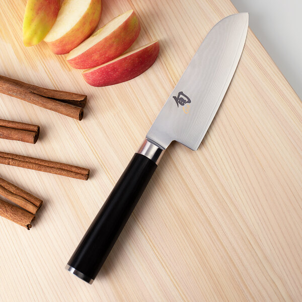 A Shun Classic Santoku knife next to sliced apples and cinnamon.
