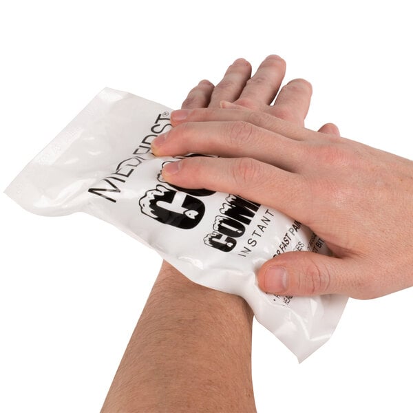 A person's hands holding a white package of Medique Medi-First Instant Ice Pack.