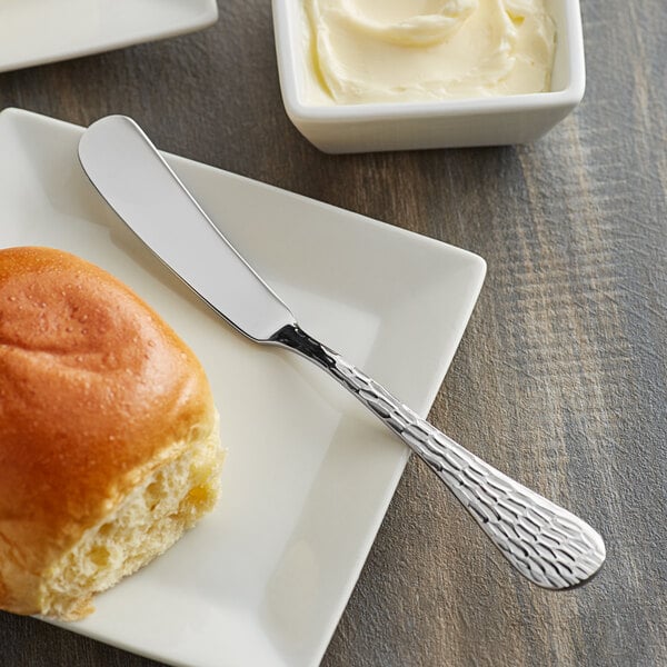 A white plate with a piece of bread and an Acopa Industry stainless steel butter knife with butter on it.