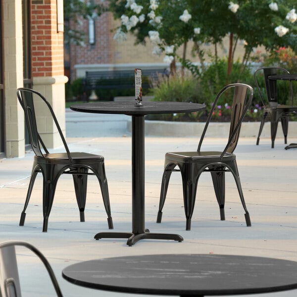 A black Lancaster Table & Seating table with a smooth round table top on a patio with black chairs.