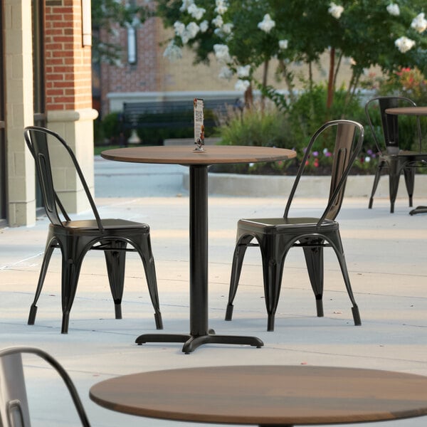 A Lancaster Table & Seating round table with a textured farmhouse finish on an outdoor patio with chairs.