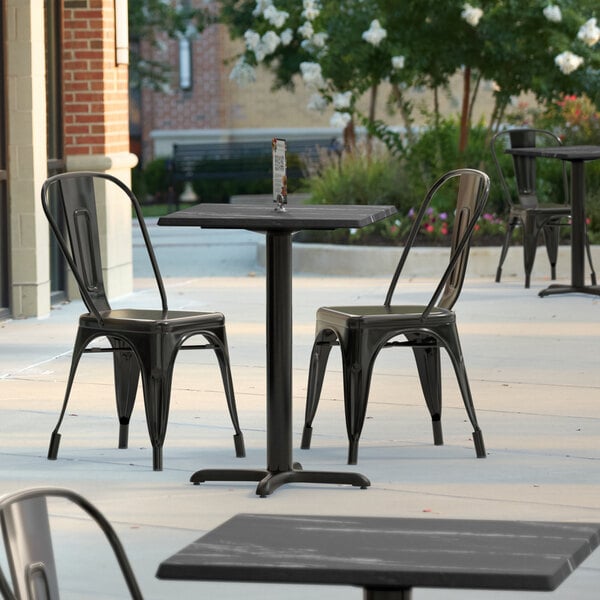 A black Lancaster Table & Seating square table top with a smooth finish on an outdoor patio with black metal chairs.