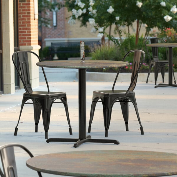 A Lancaster Table & Seating Excalibur round table top with a textured canyon metal finish on a patio with chairs.