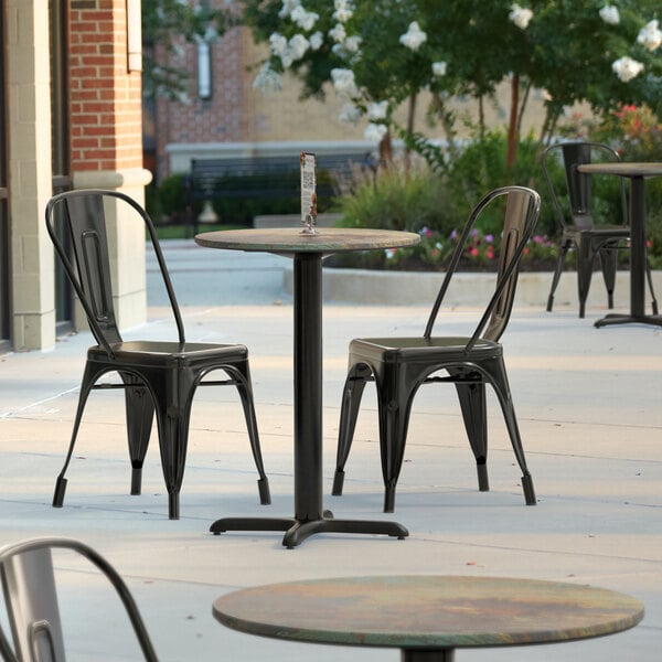 A Lancaster Table & Seating round table with a textured metal finish on a patio with chairs and flowers.