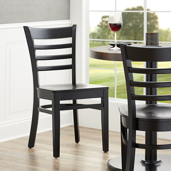 A Lancaster Table & Seating black wood ladder back chair with a black seat at a table in a restaurant.