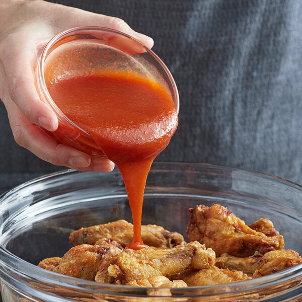 A person pouring Frank's RedHot Sriracha Chili Sauce into a bowl of chicken wings.