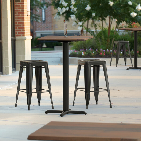 A Lancaster Table & Seating square counter height table with a textured farmhouse finish and cross base plate on a patio with three stools.
