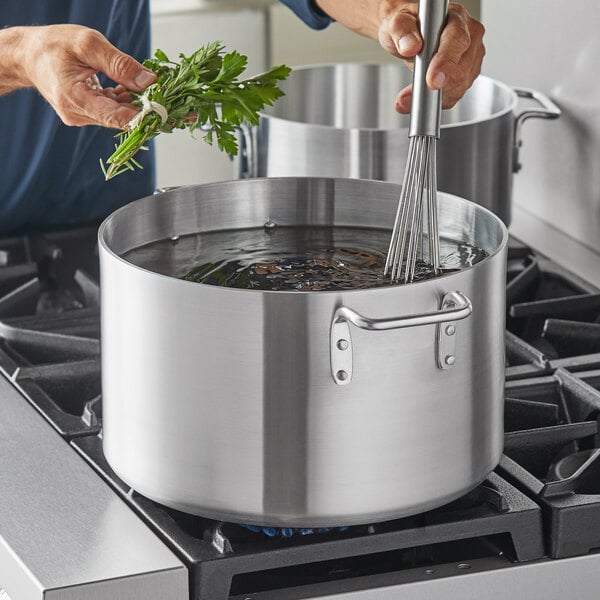 A person cooking food in a Choice aluminum sauce pot on a stove.