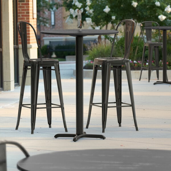 A Lancaster Table & Seating Excalibur bar height table with black chairs on a patio.