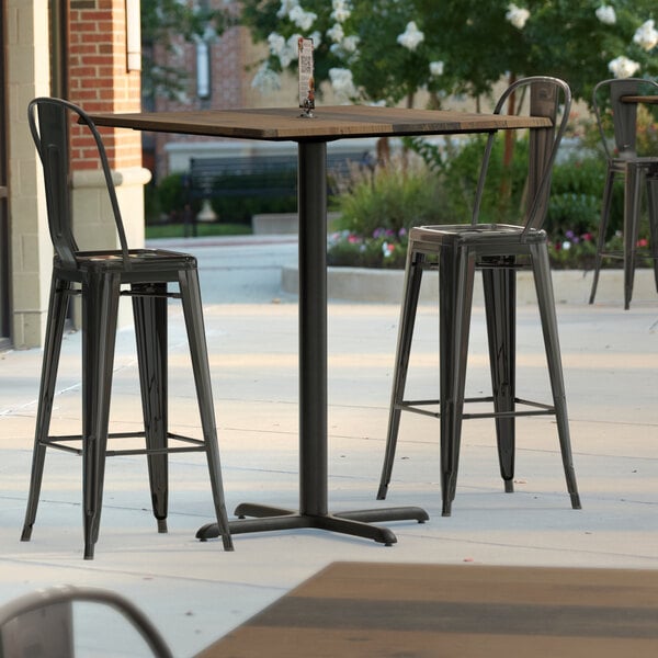 A Lancaster Table & Seating bar height table with a textured farmhouse finish on a patio with chairs.