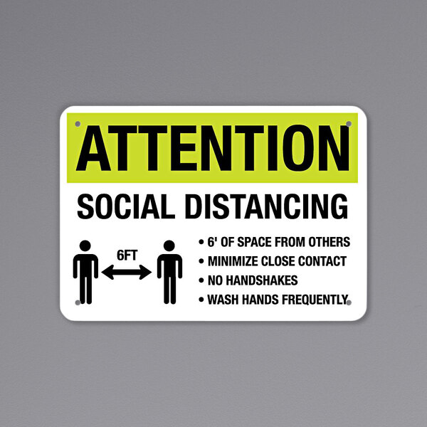 A black and yellow reflective sign that says "Attention / Social Distancing" with a symbol of people standing 6 ft apart.
