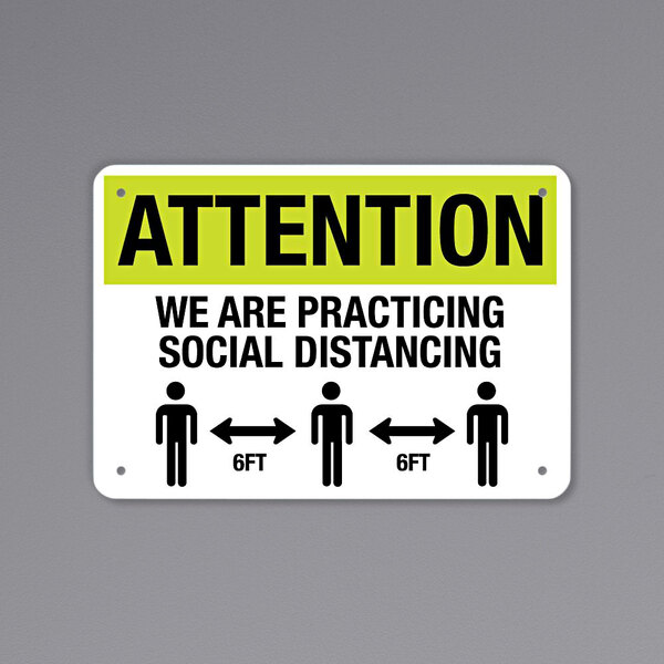 A black and yellow aluminum sign with people icons and text that says "Attention / We Are Practicing Social Distancing / 6 Ft."