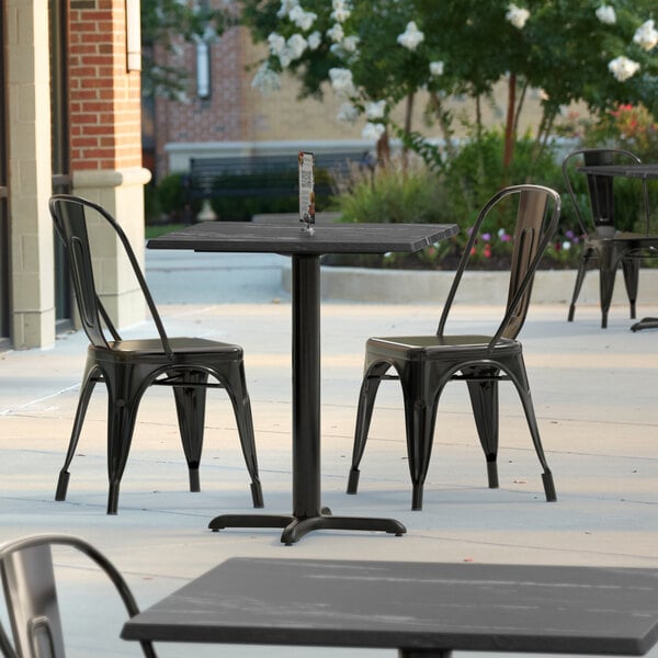 A Lancaster Table & Seating Excalibur dining table with a black metal cross base plate on a patio.