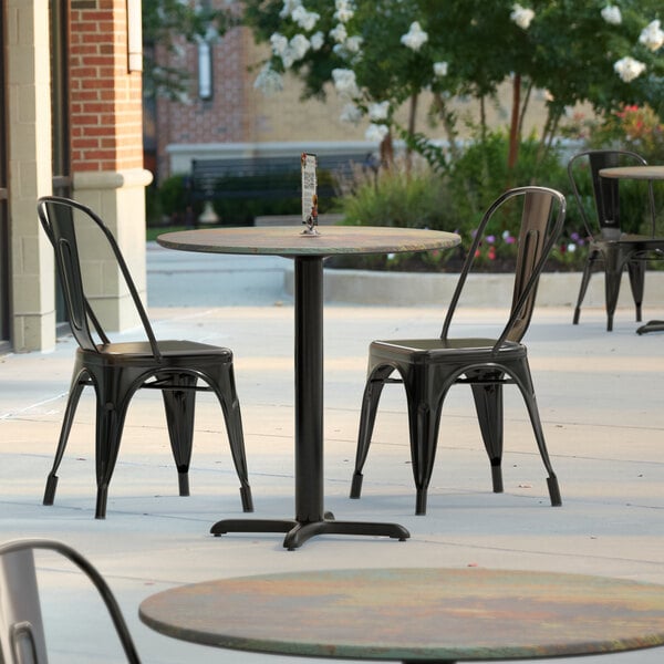 A Lancaster Table & Seating Excalibur round outdoor dining table with a textured metal finish and cross base plate on an outdoor patio.