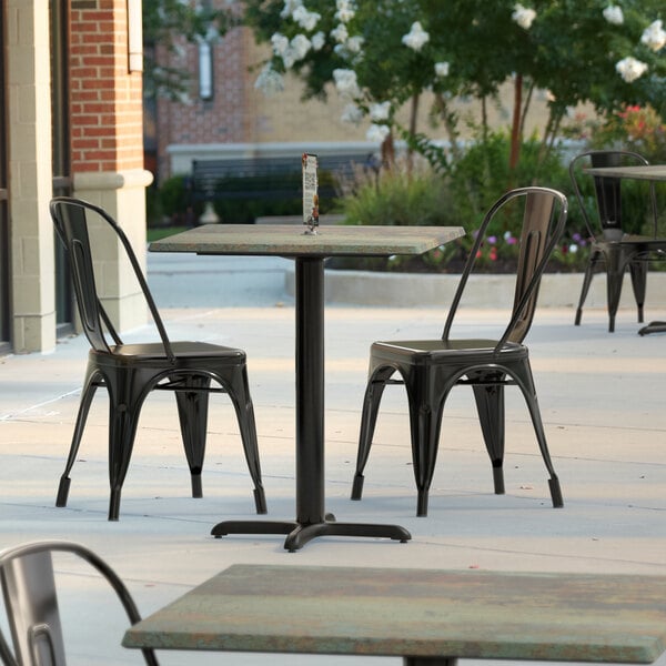 A Lancaster Table & Seating Excalibur square dining table with a textured metal finish and cross base plate on a patio.