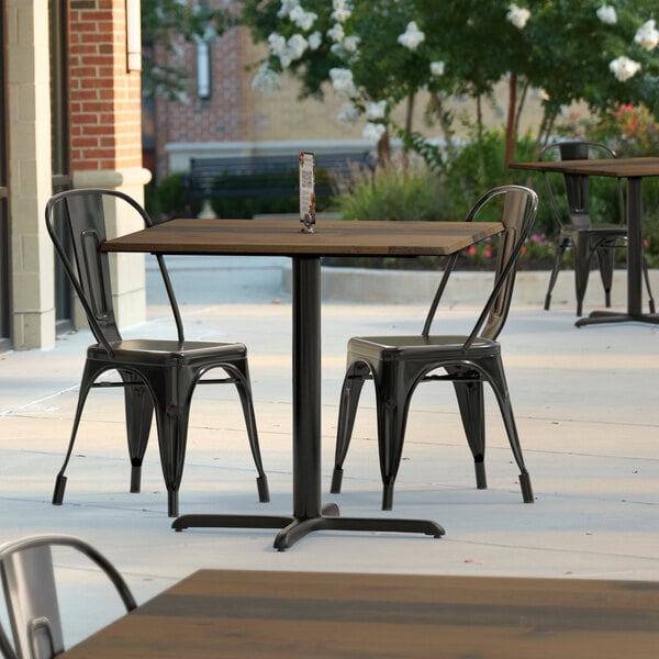 A Lancaster Table & Seating square dining table with a textured finish and cross base on a patio.