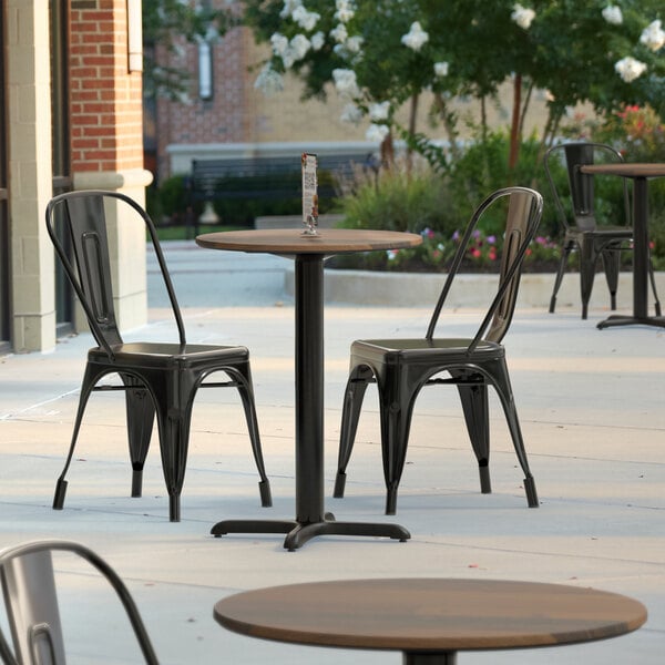 A black chair and a Lancaster Table & Seating round dining table with a textured farmhouse finish on a patio.
