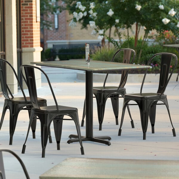 A Lancaster Table & Seating rectangular dining table with a textured metal finish and cross base plate on a patio.
