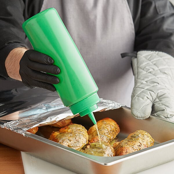 A person in a black glove using a Choice green wide mouth squeeze bottle to pour sauce on food.