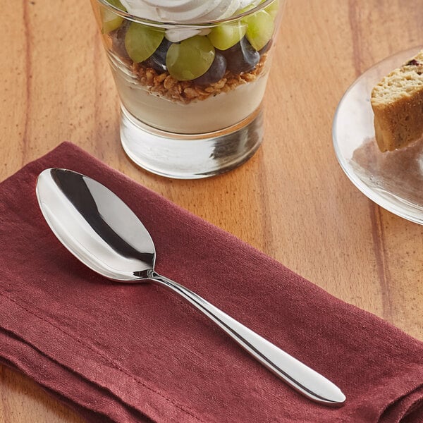 An Acopa Remy stainless steel dinner spoon on a napkin next to a dessert.