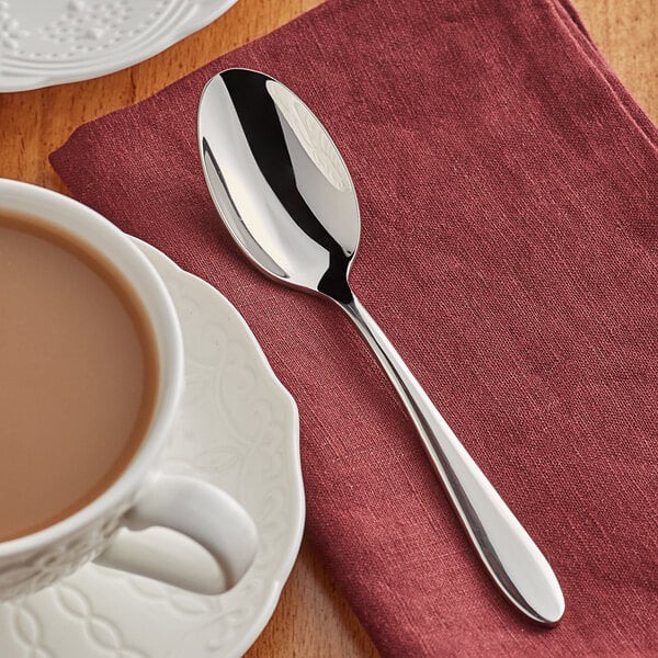 An Acopa Remy stainless steel teaspoon on a napkin next to a cup of coffee.