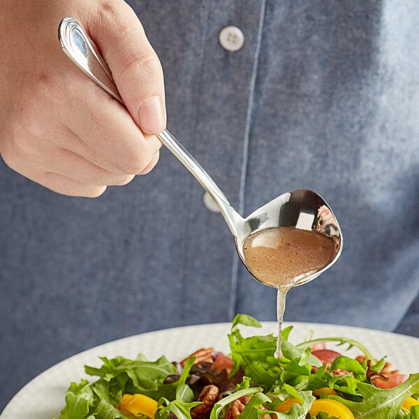 A person using an Acopa stainless steel ladle to serve liquid over a salad.