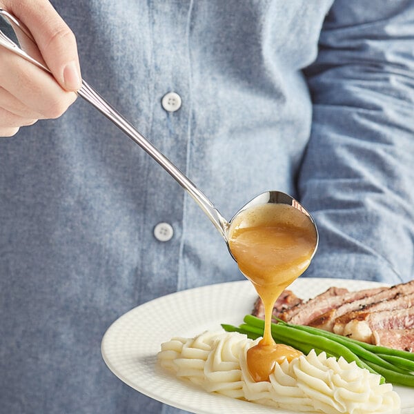 A person using an Acopa stainless steel ladle to pour gravy over a plate of food.