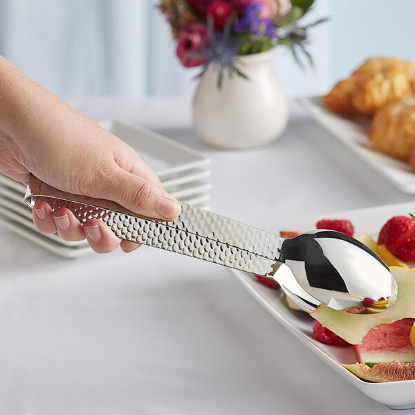 A person using Acopa Industry stainless steel serving tongs to put fruit on a plate.