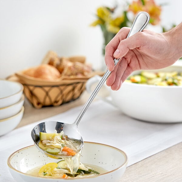 A hand using an Acopa stainless steel ladle to spoon soup into a bowl.