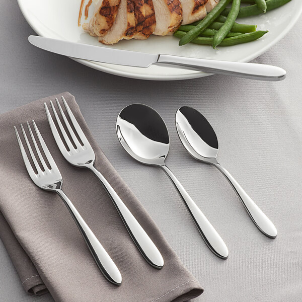 Acopa Remy 18/8 stainless steel flatware on a table with a fork and spoon on a napkin.