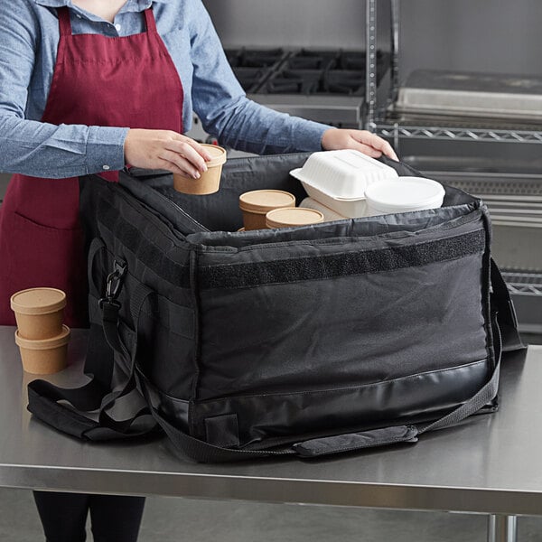 A woman in a red apron putting containers of food into a Vesture heavy-duty large thermal catering bag.