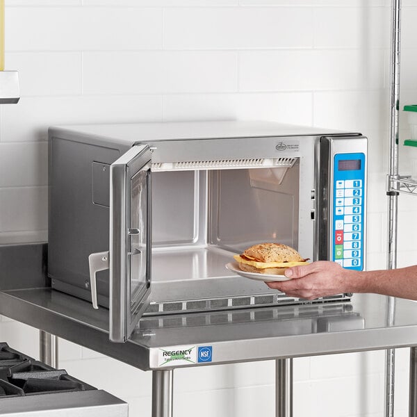 A person holding a plate of food in a Solwave stainless steel commercial microwave.