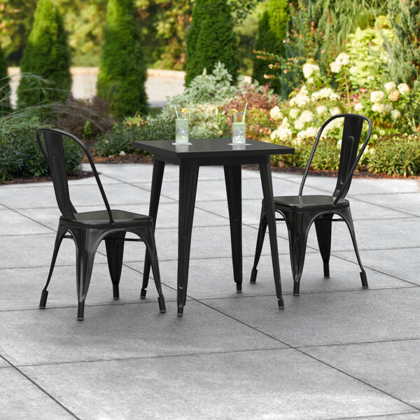 A Lancaster Table & Seating black outdoor table with 2 black metal chairs on a patio.