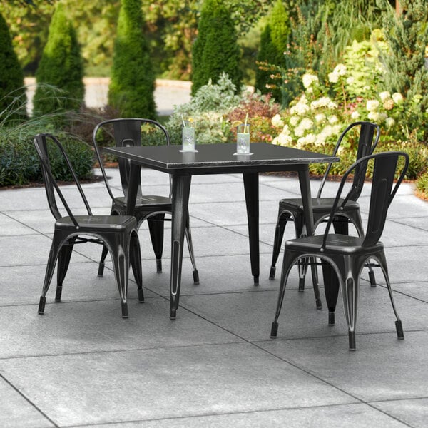 A Lancaster Table & Seating distressed black metal outdoor table with 4 chairs on an outdoor patio.