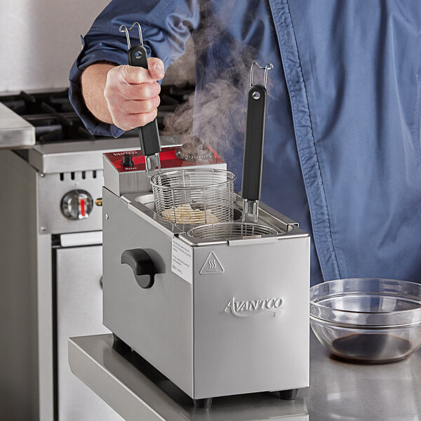 A man using an Avantco countertop electric pasta cooker to cook food on a counter in a professional kitchen.
