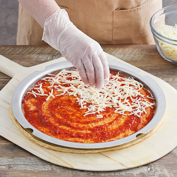 A person using a Vollrath aluminum pizza sauce portion ring to put cheese on a pizza.