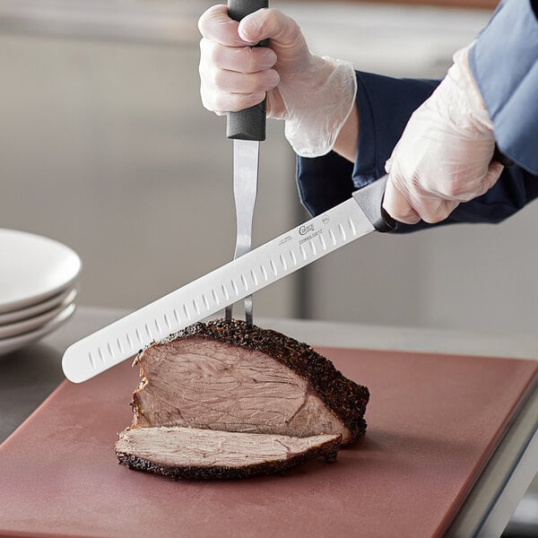 A person using a Choice Granton Edge Slicing Knife to cut a piece of meat.