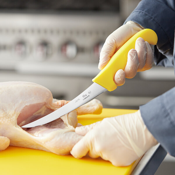 A person using a Choice 6" curved stiff boning knife with a yellow handle to cut chicken.