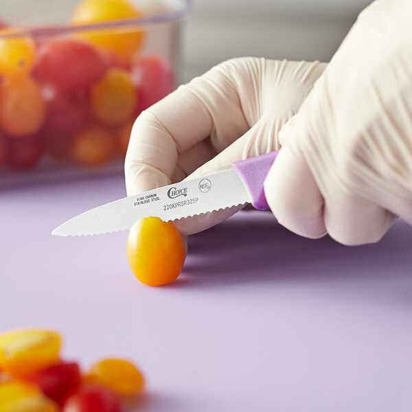 A person in gloves using a Choice serrated paring knife to cut a tomato.