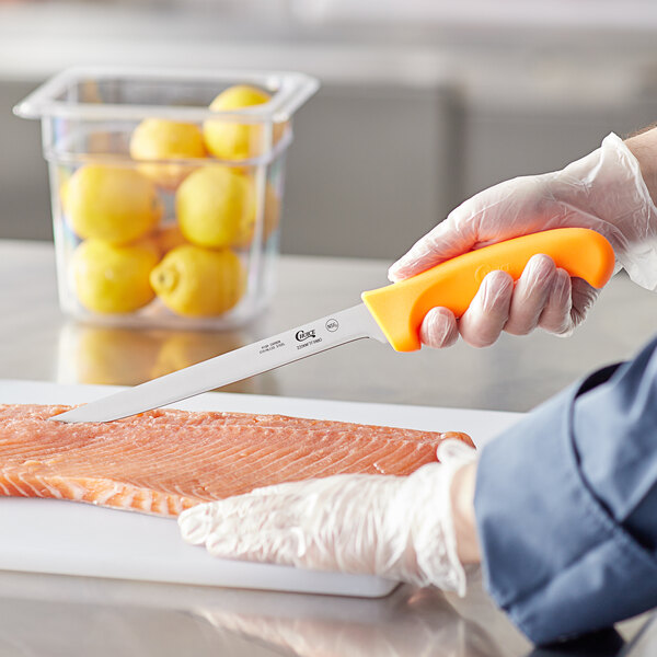 A person cutting a piece of fish with a Choice 8" Narrow Semi-Stiff Fillet Knife with a neon orange handle.