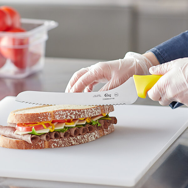 A person using a Choice yellow offset bread knife to cut a sandwich.