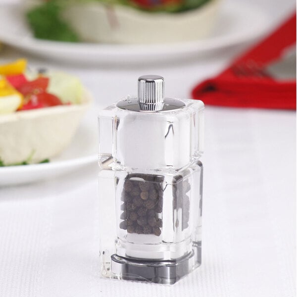A Chef Specialties cubic acrylic pepper mill with a glass lid on a table.