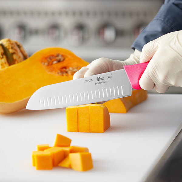 A person using a Choice Santoku knife with a neon pink handle to cut a pumpkin.